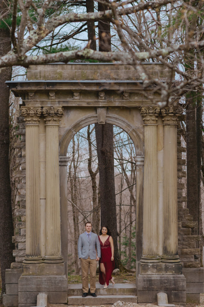 engaged couple standing under old ruins of an arch