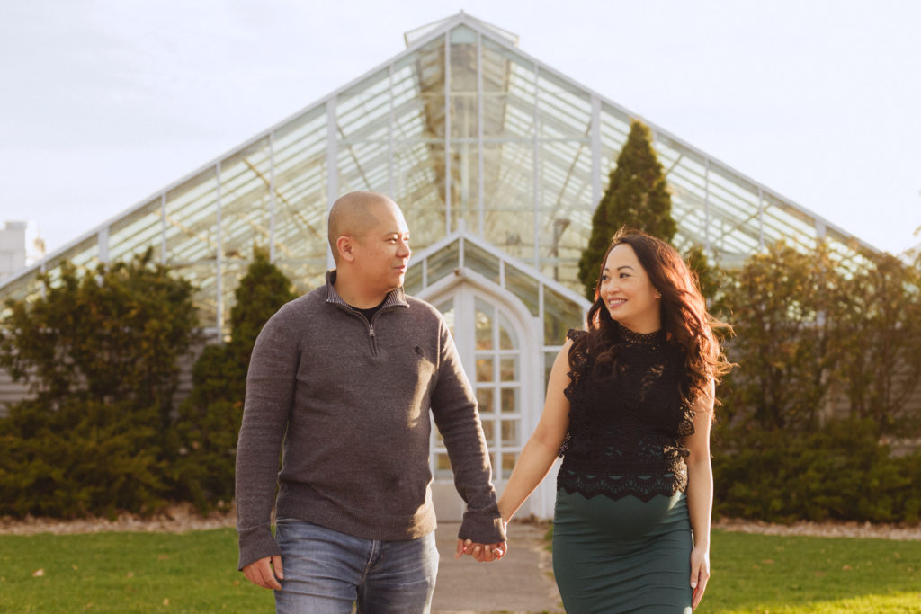 expecting parents holding hands in front of greenhouse