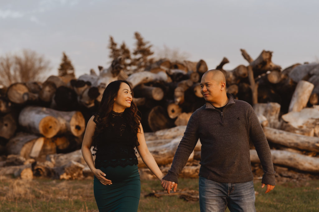 expecting parents holding hands in front of log pile