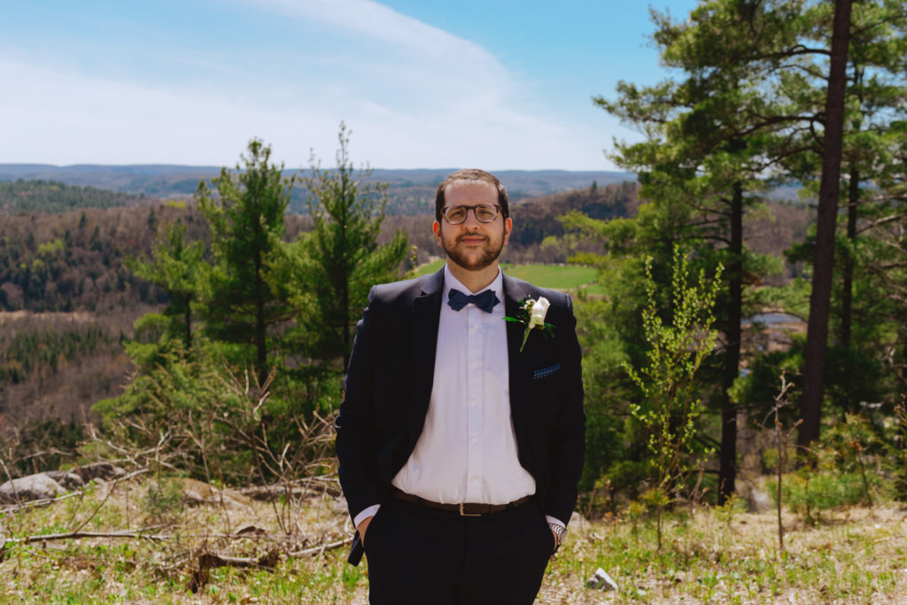 Groom standing on top of a cliff overlooking the Gatineau hills