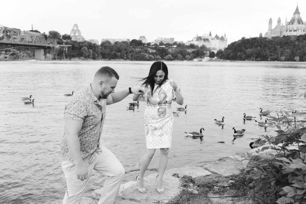 man helping his fiancee as she steps off a rock in her high heels