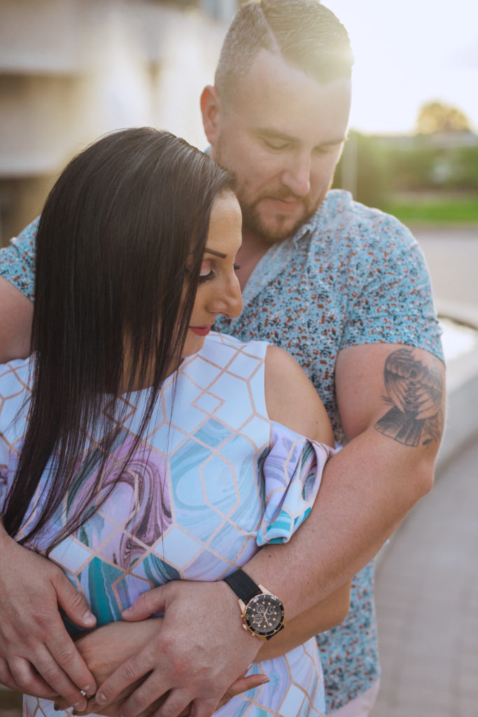 engaged couple cuddling together at sunset