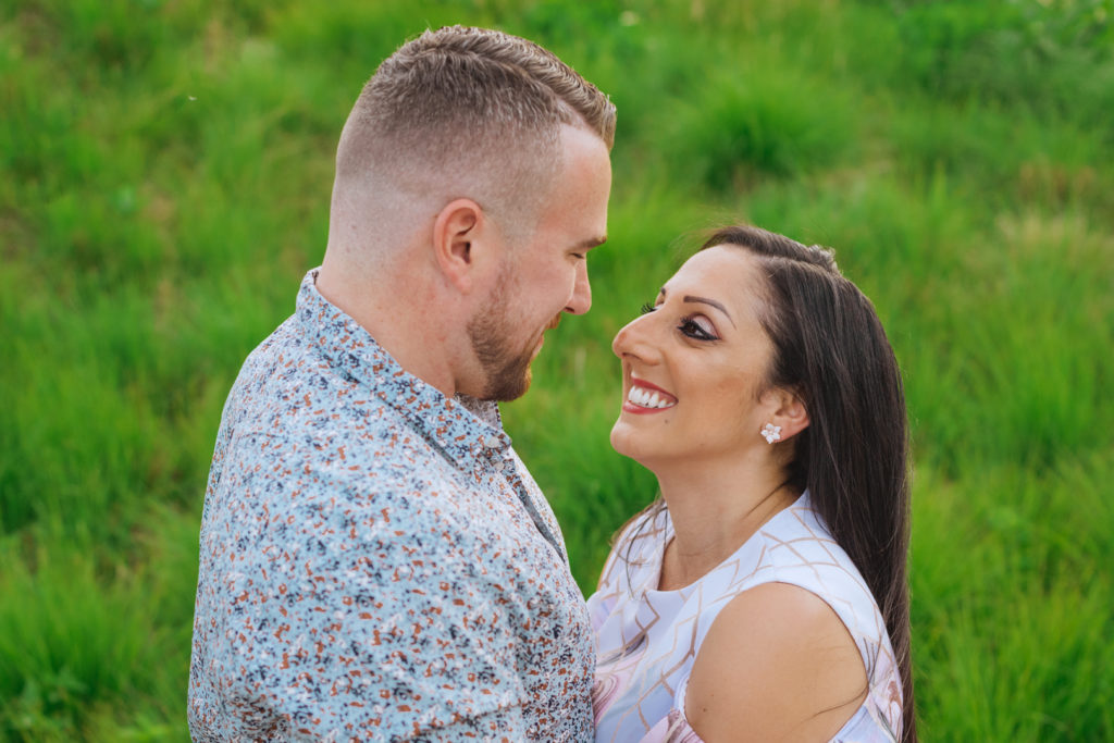 engaged couple smiling together with tall green grass in the background