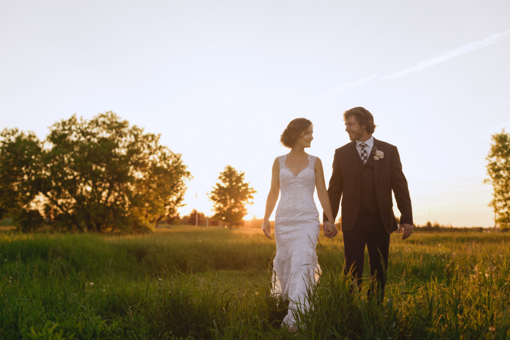 bride and groom walking through tall grass at sunset