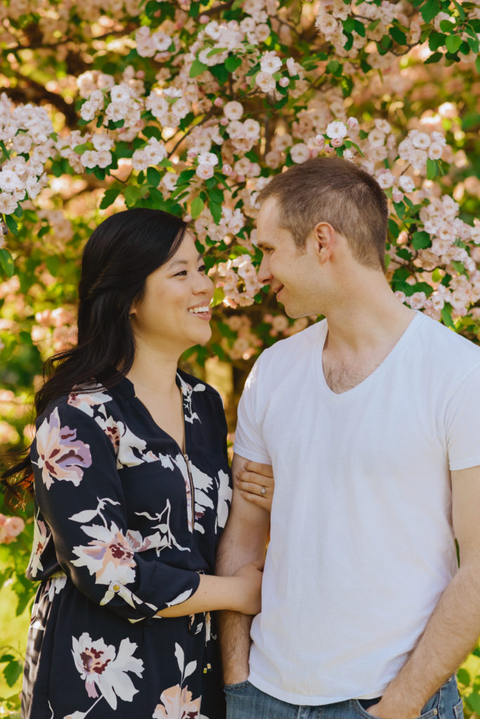 engaged couple smiling at each other in front of cherry blossom tree