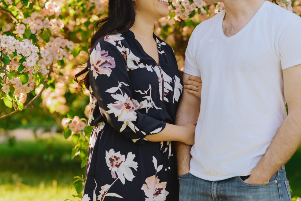 engaged couple cuddling in front of cherry blossom tree