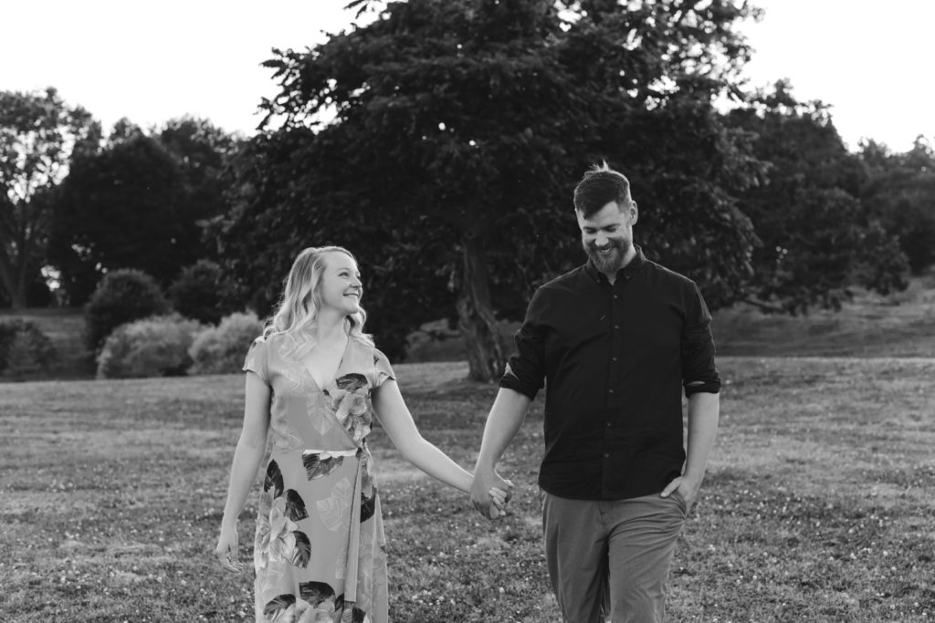 black and white photo of engaged couple holding hands walking through a field