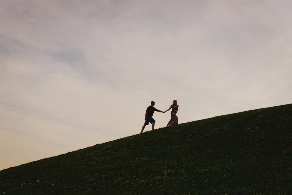 silhouette of engaged couple holding hands walking up a hill