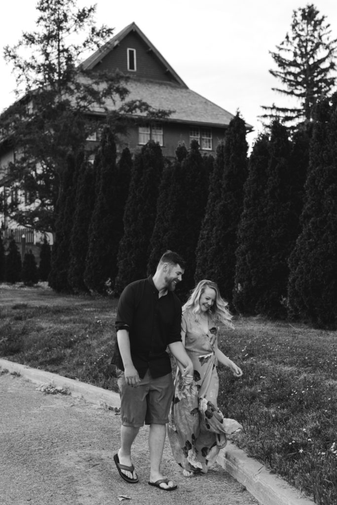 black and white photo of engaged couple walking down a path laughing