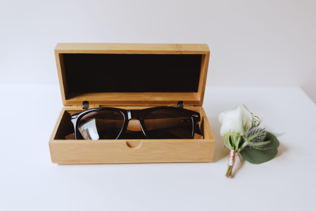 groom's sunglasses and boutenniere on white table