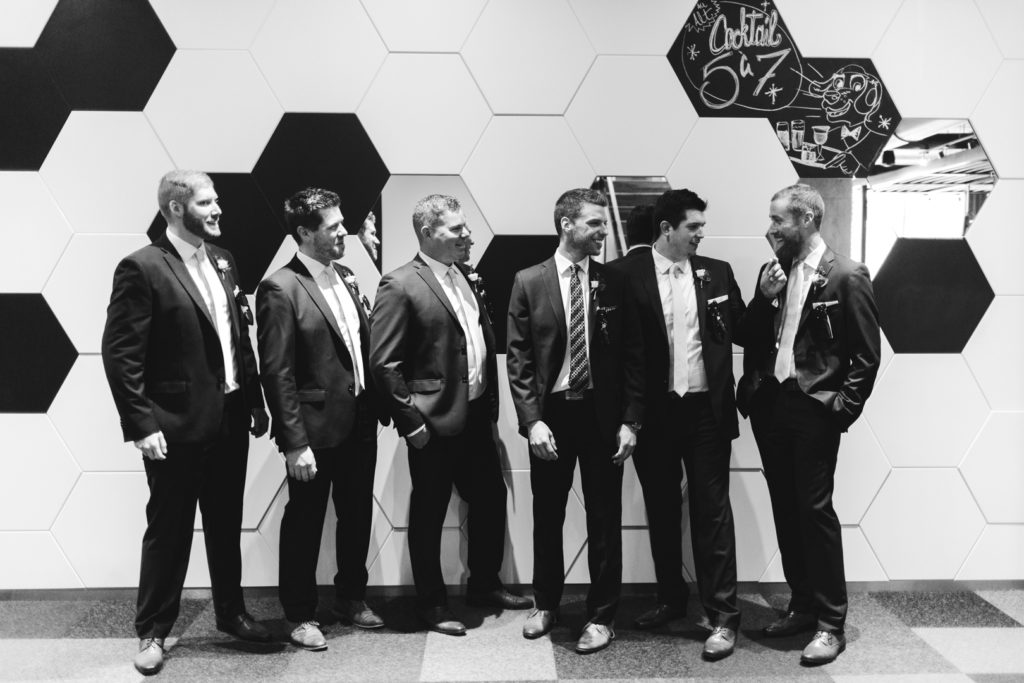 groom and groomsmen standing in front of black and white mosaic wall laughing