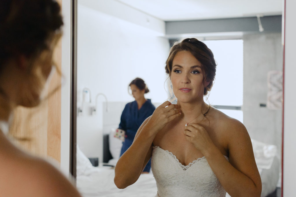 bride putting on her necklace in front of the mirror