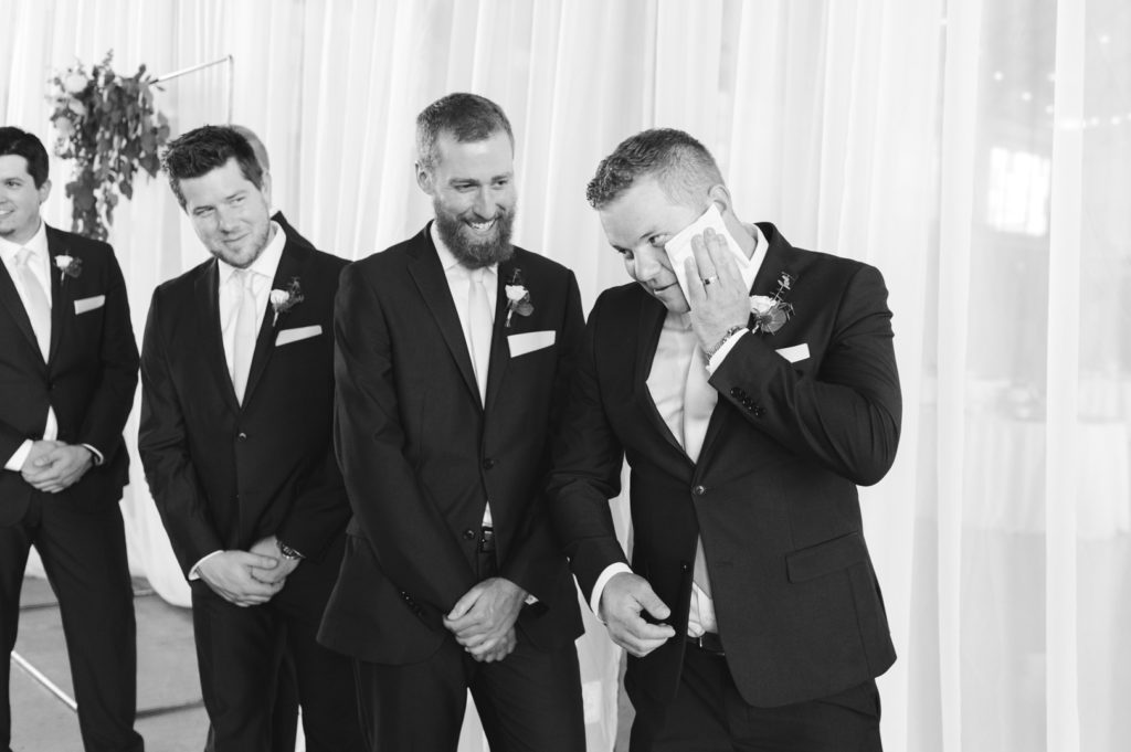 groomsman wiping his sweaty face with a cocktail napkin during the ceremony