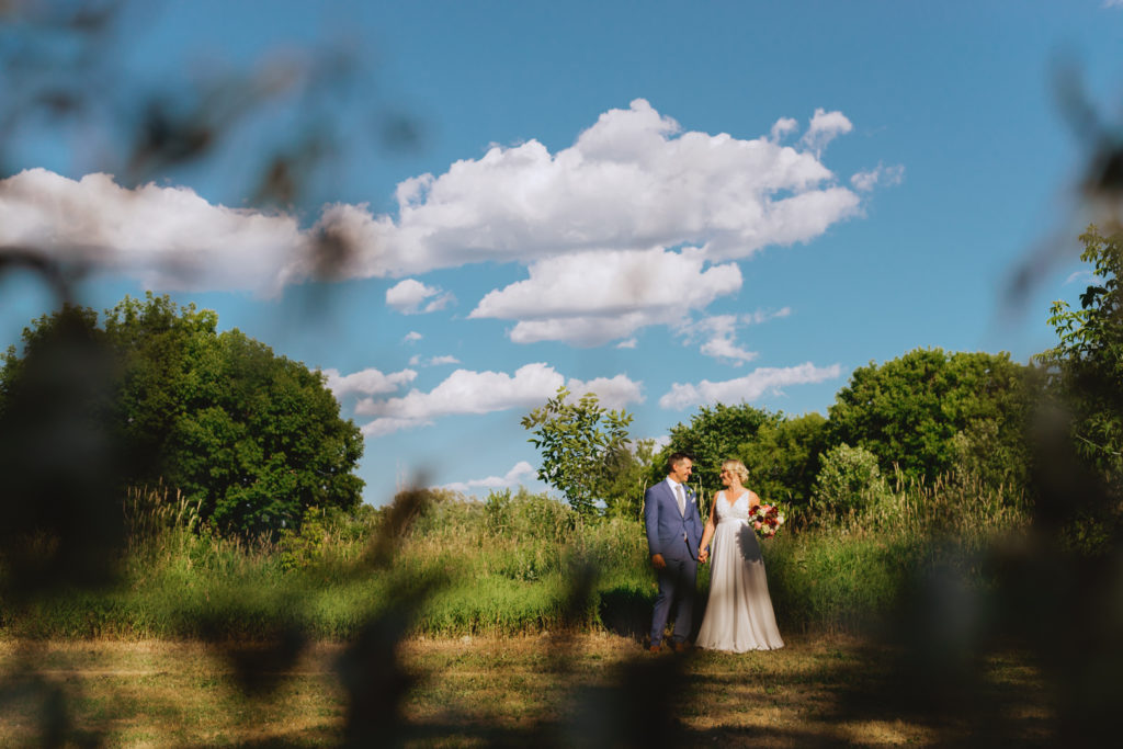 bride and groom standing in a sunny field holding hands
