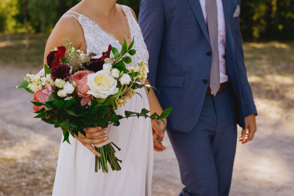 bride and groom holding hands walking down a path holding bridal bouquet from Pollen Nation