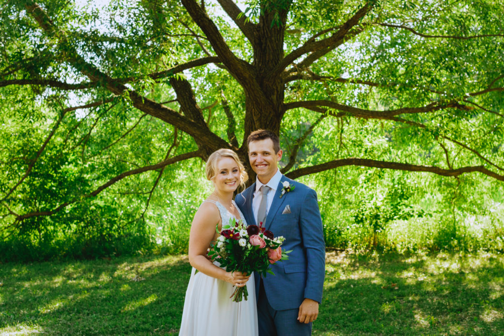 bride and groom standing underneath a tree smiling for the camera