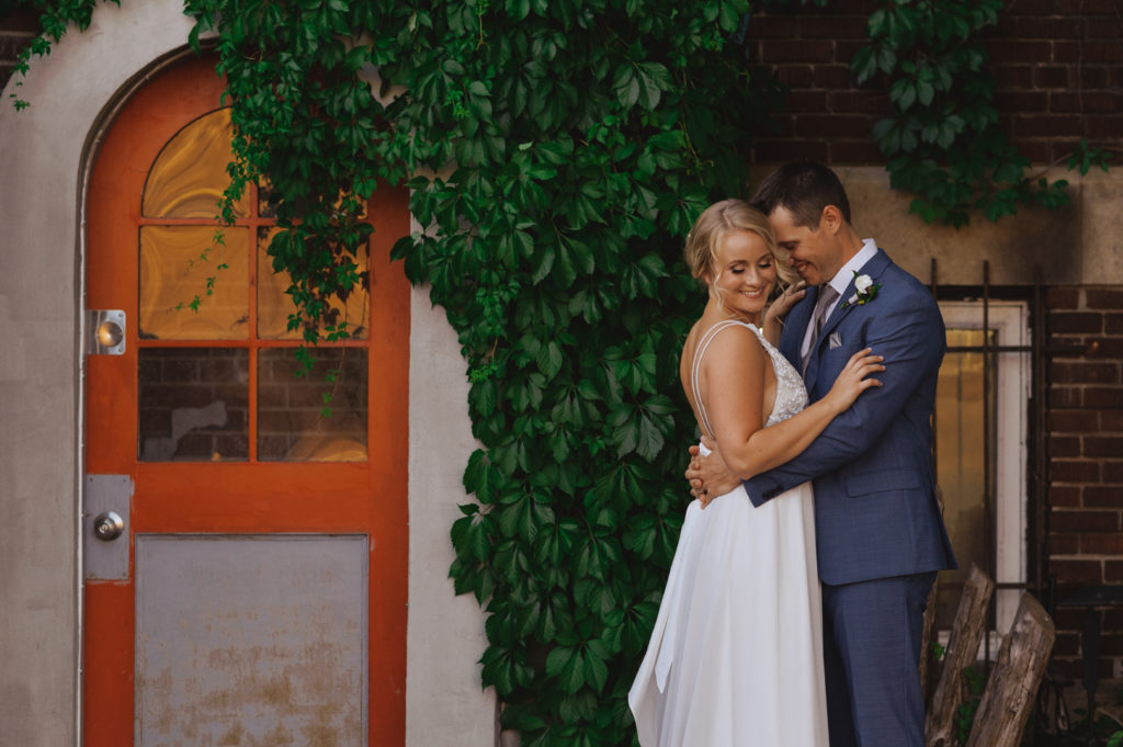 bride and groom next to orange door and vines cuddling
