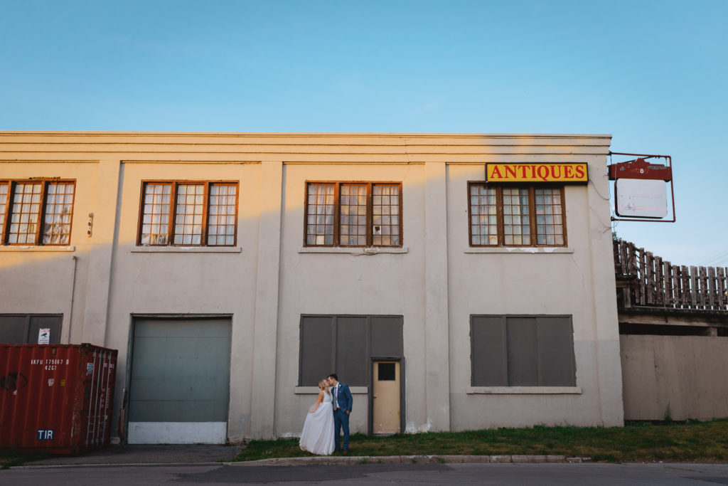 bride and groom kissing in front of old industrial building with antique sign