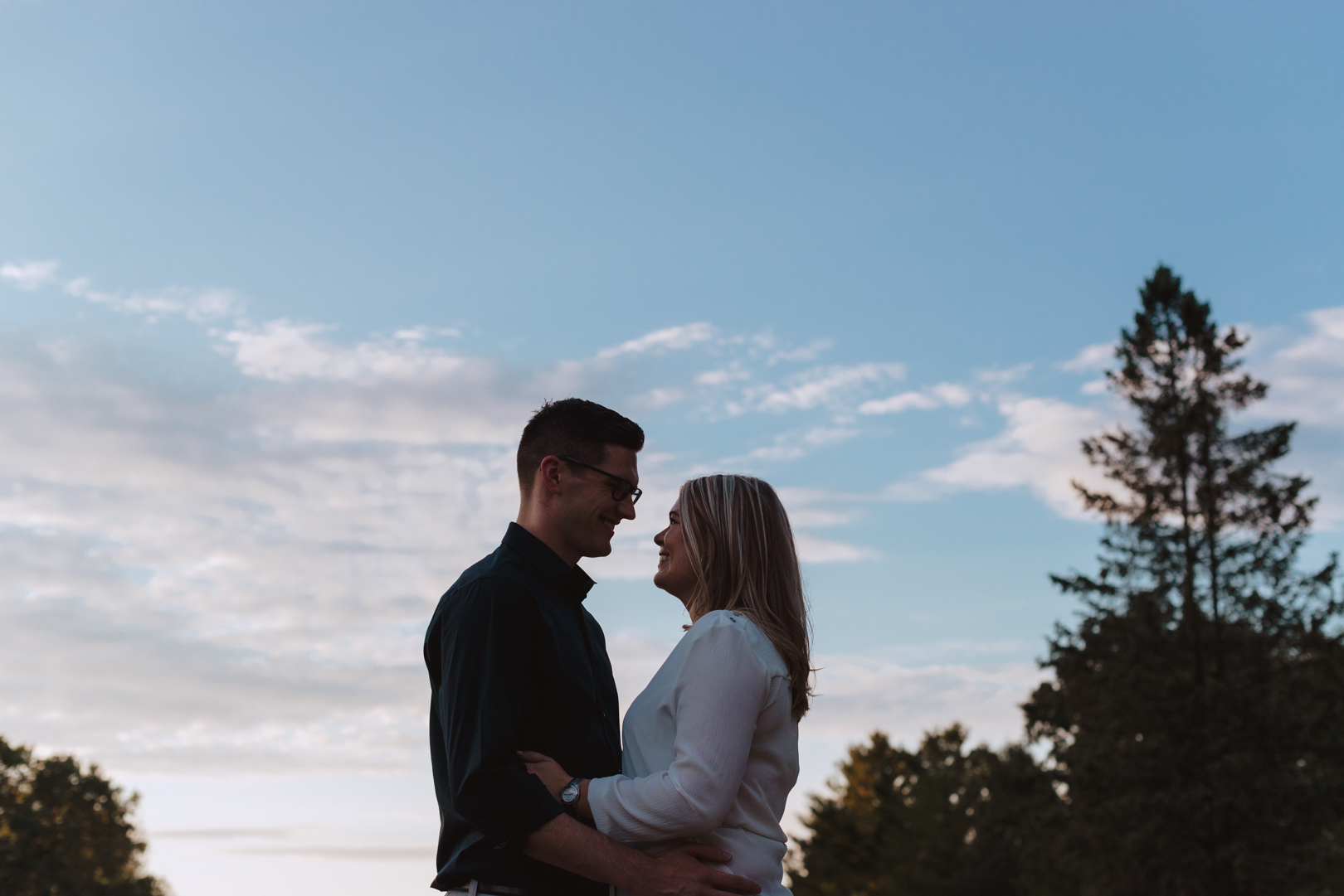 engaged couple smiling at each other with blue sunset sky in the background