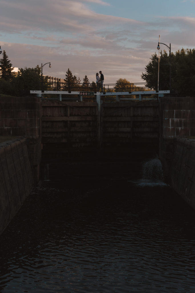 engaged couple silhouetted standing on locks of the rideau canal at sunset