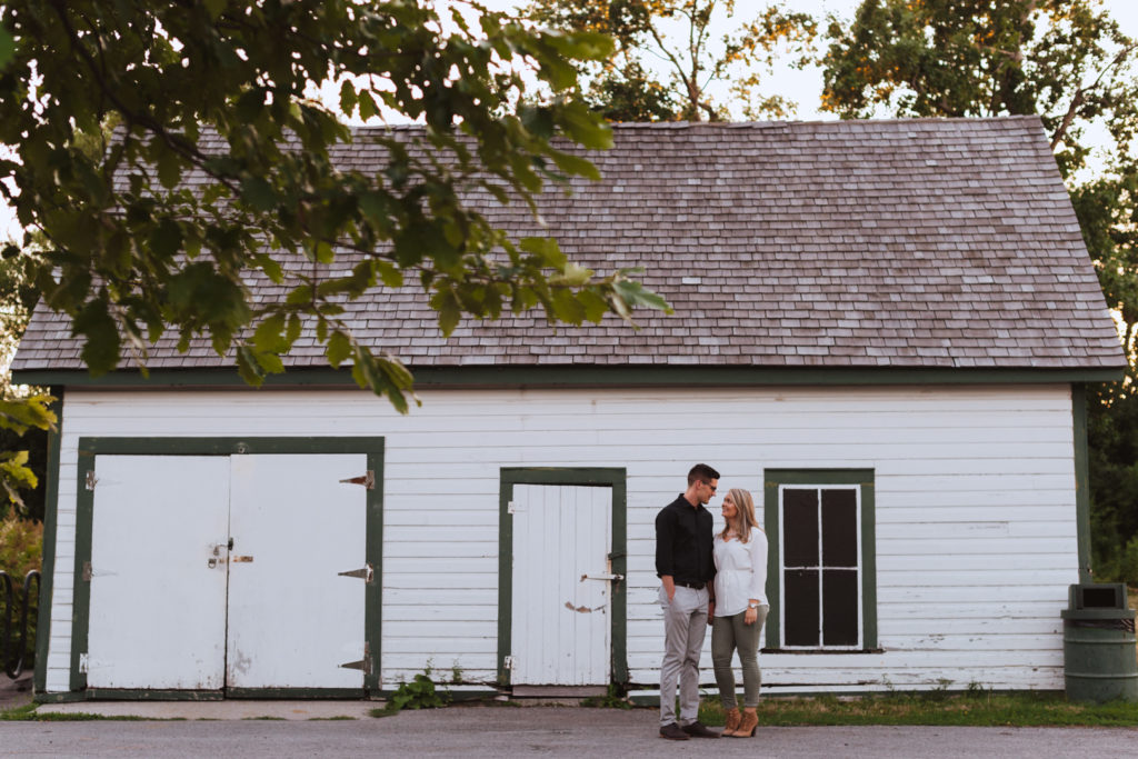 engaged couple standing in front of white and green garage holding hands