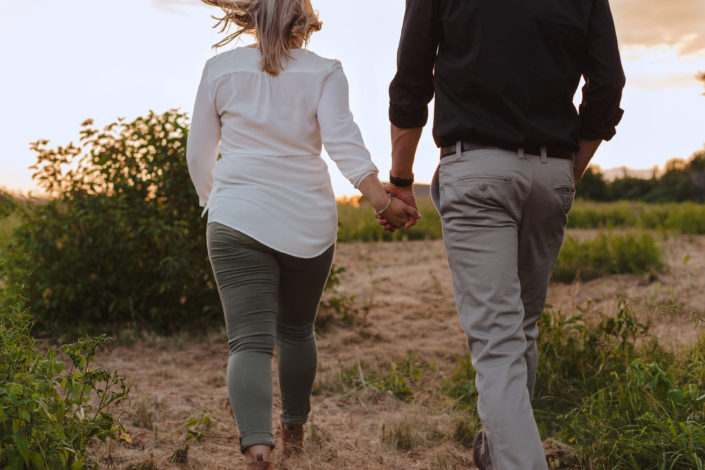 engaged couple walking in a field at sunset holding hands