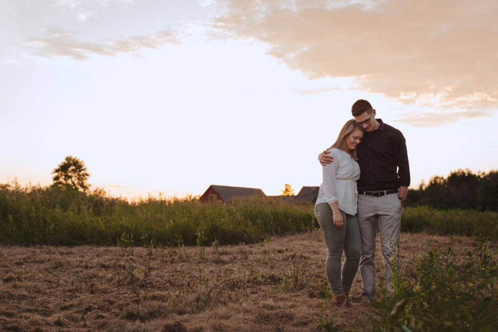engaged couple cuddling in a farmer's field at sunset holding hands