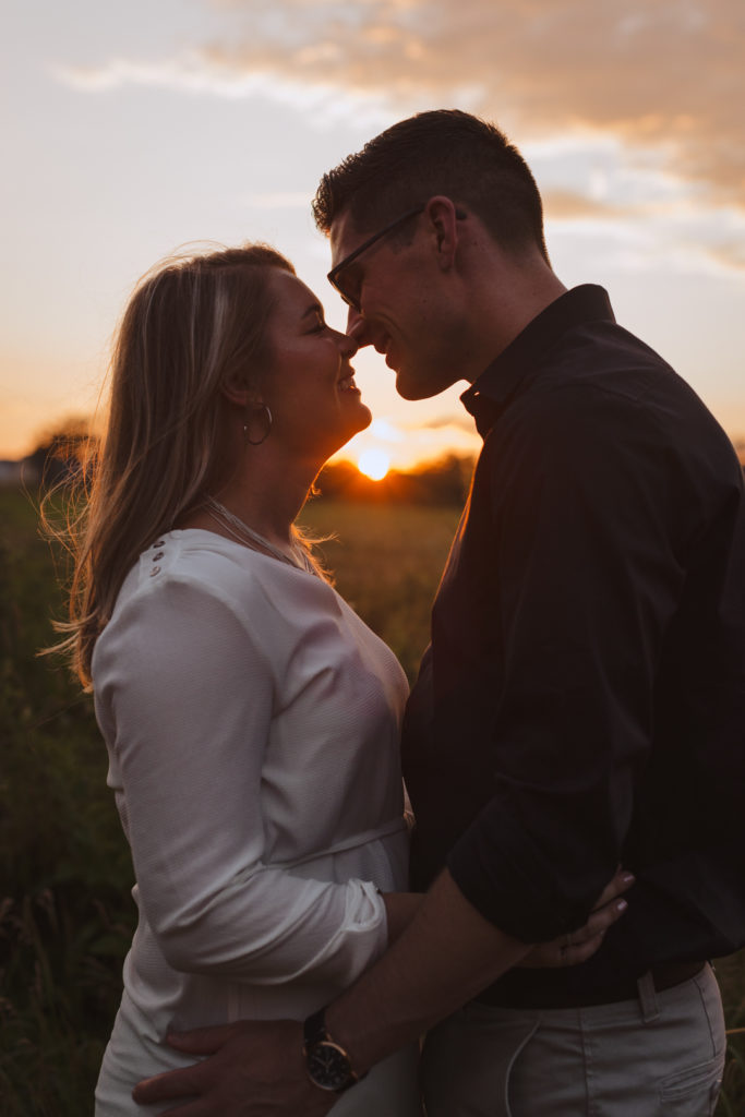 engaged couple cuddling in a farmer's field at sunset about to kiss
