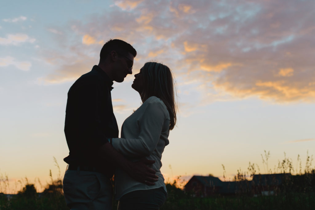 engaged couple cuddling in a farmer's field at sunset about to kiss