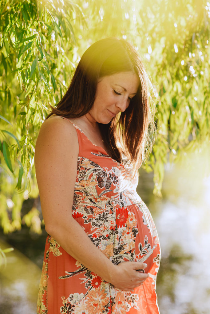mom to be underneath willow tree smiling at belly