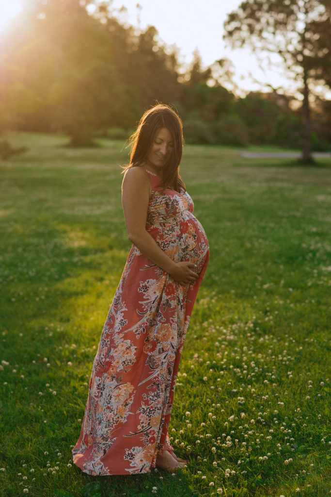 mom to be smiling at her belly in a pink flowy dress at sunset