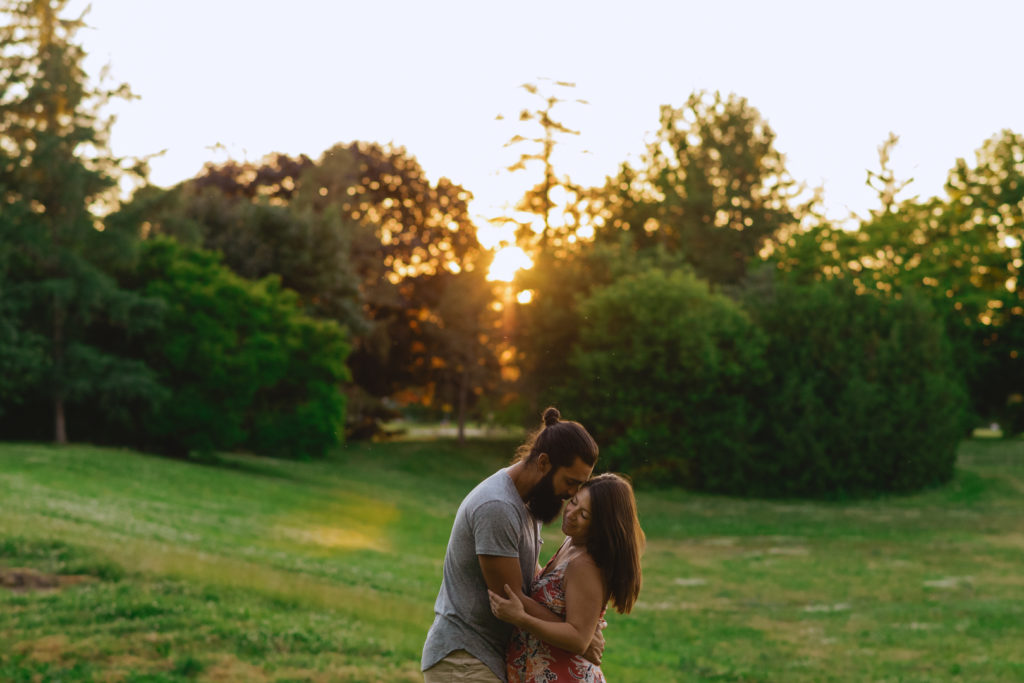 expecting parents cuddling in a field at sunset
