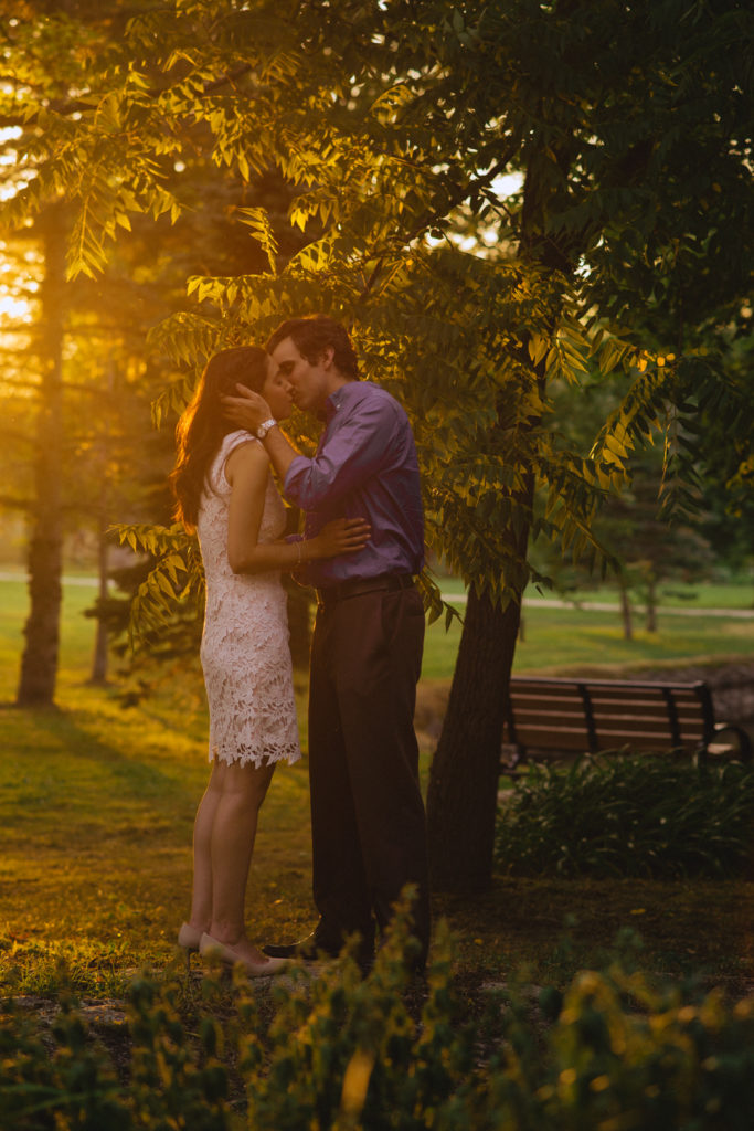 engaged couple kissing among the trees at golden hour