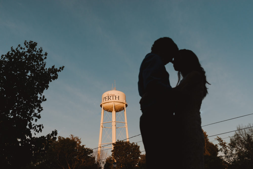 engaged couple cuddling at sunset with Perth water tower in the background