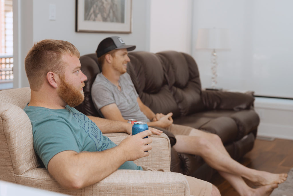 groom and groomsman drinking beer watching soccer on the couch