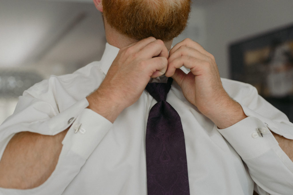 groom adjusting his purple tie