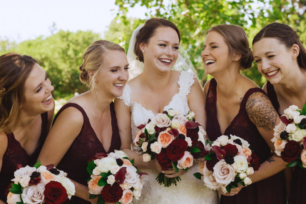 bride and bridesmaids laughing holding red and white bouquets