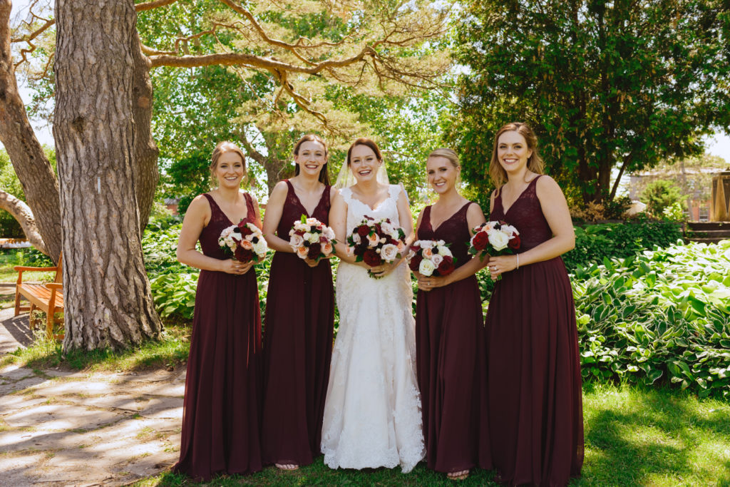 bride and bridesmaids standing under a tree laughing and smiling at the camera