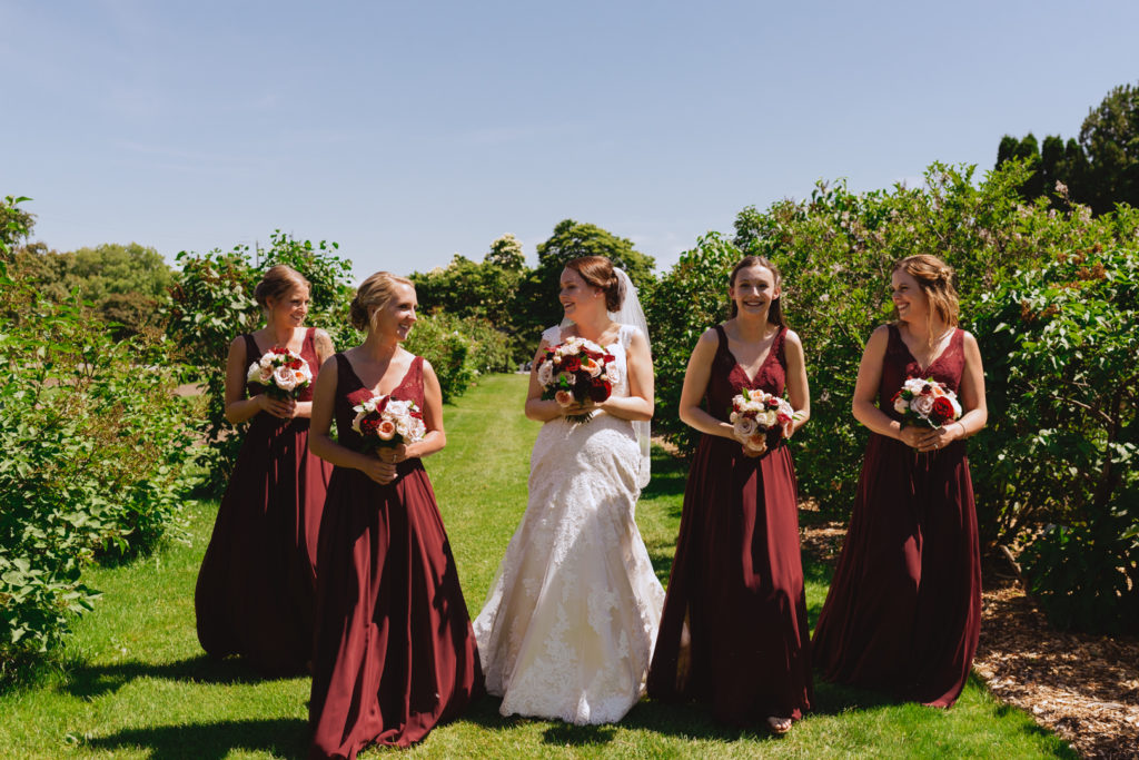 bride and bridesmaids in red walking down tree lined path in the Ornamental Gardens