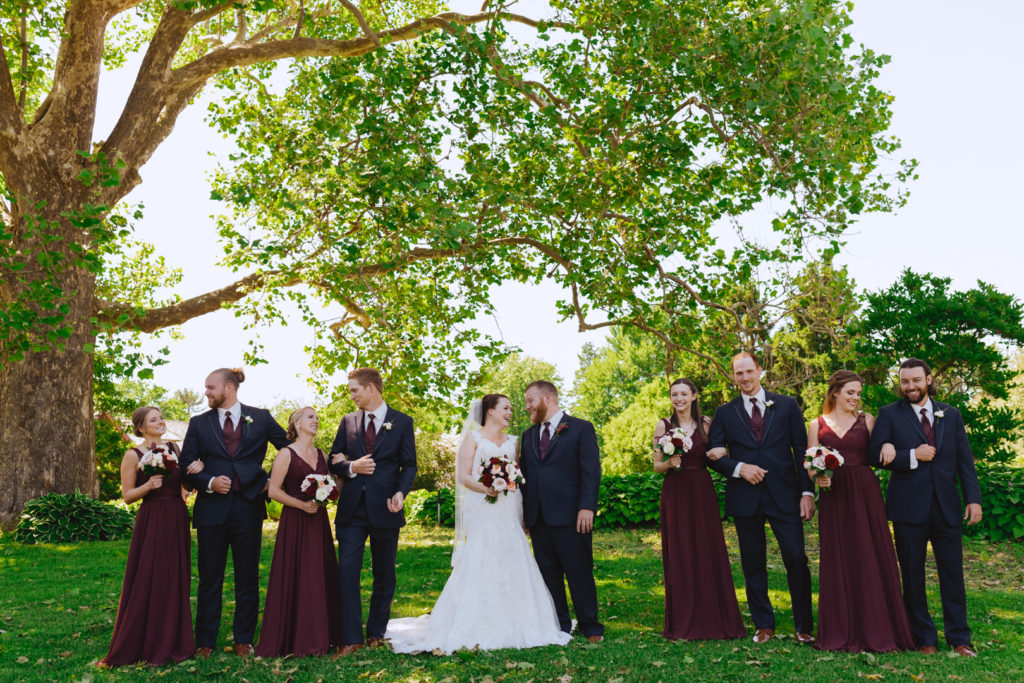 wedding party in marsala coloured dresses standing under tree in the Ornamental Gardens at the Experimental Farm