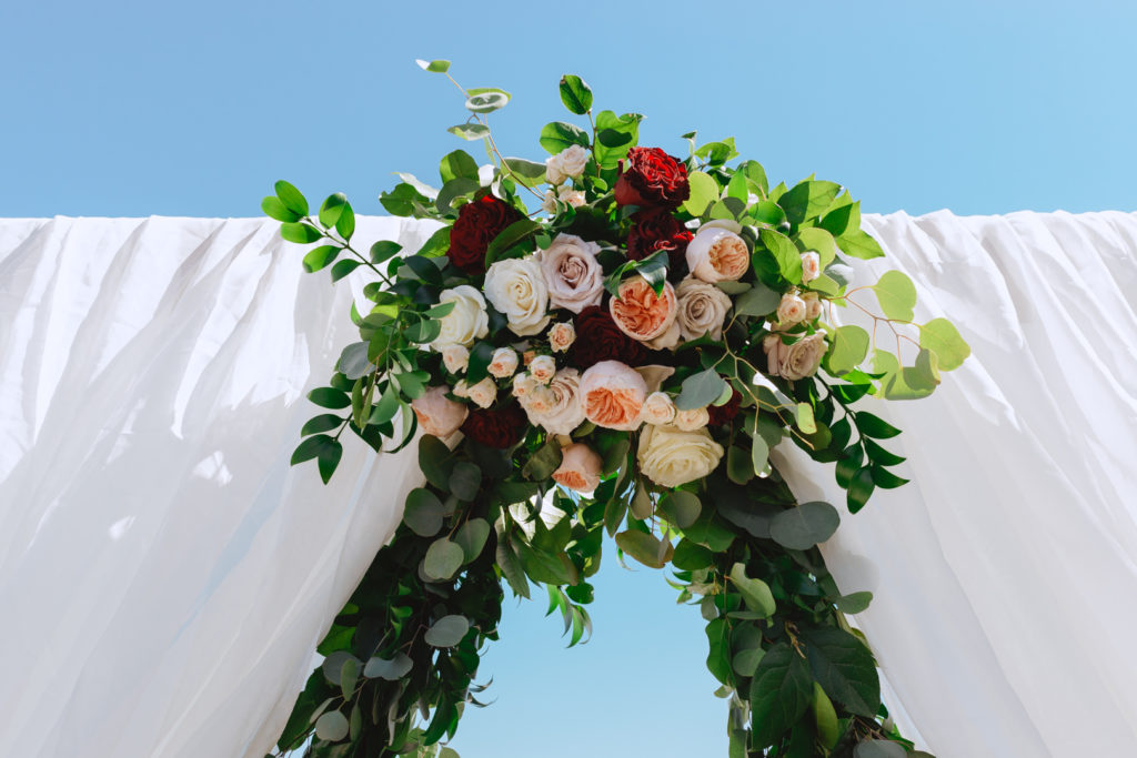 red and blush roses with greenery on top of arch at the end of the aisle