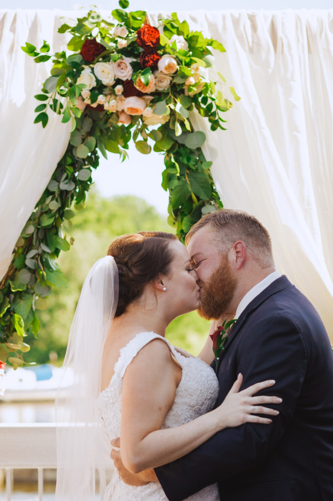 bride and groom first kiss under floral alter
