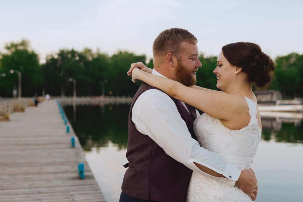 bride and groom cuddling by water at dows lake during sunset