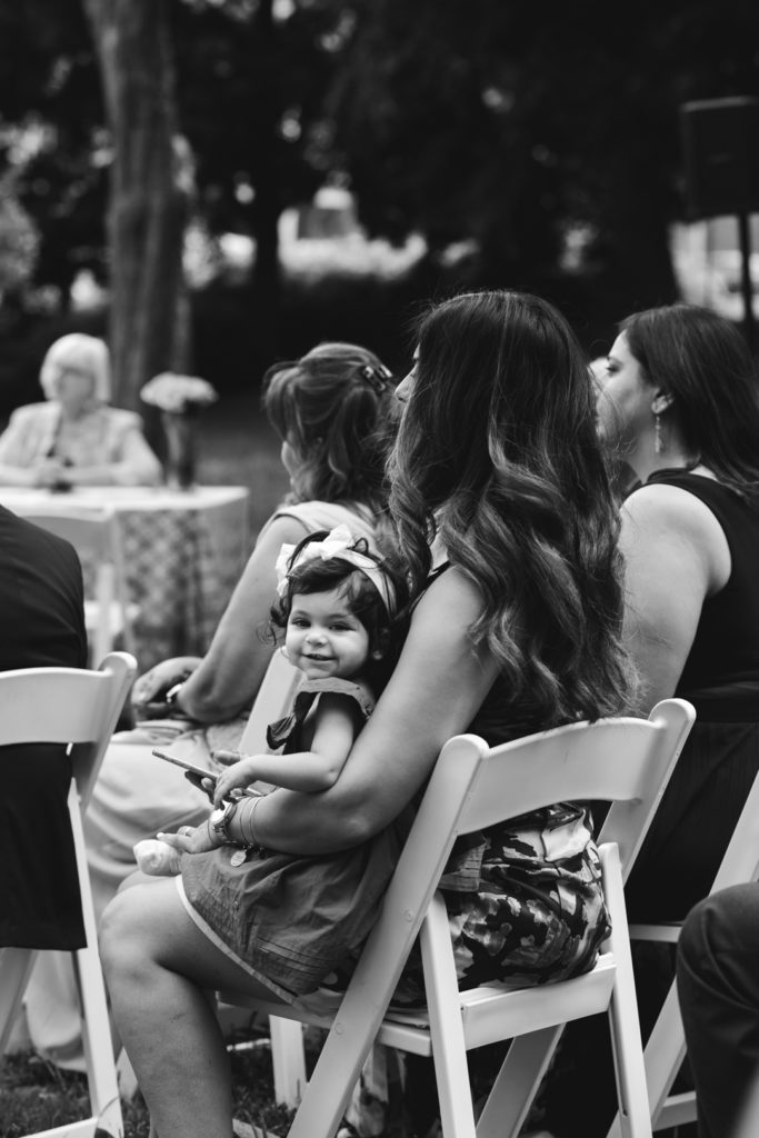flower girl sitting on her mom's lap during the ceremony smiling