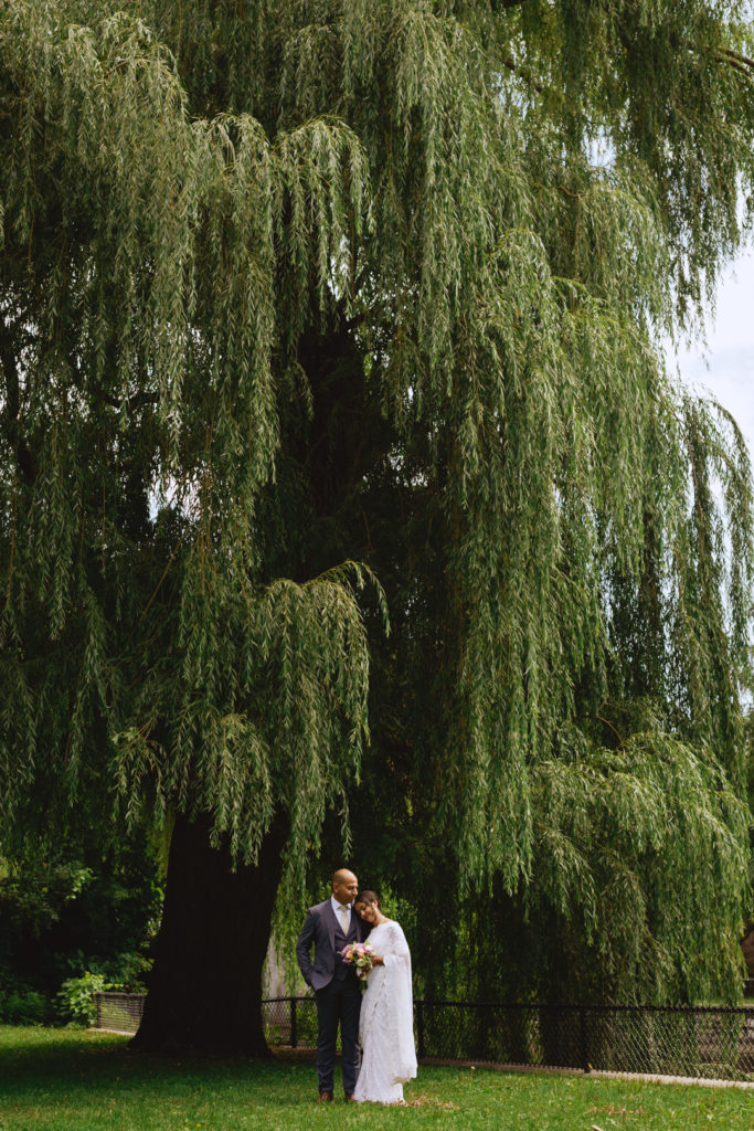 bride and groom standing underneath a willow tree