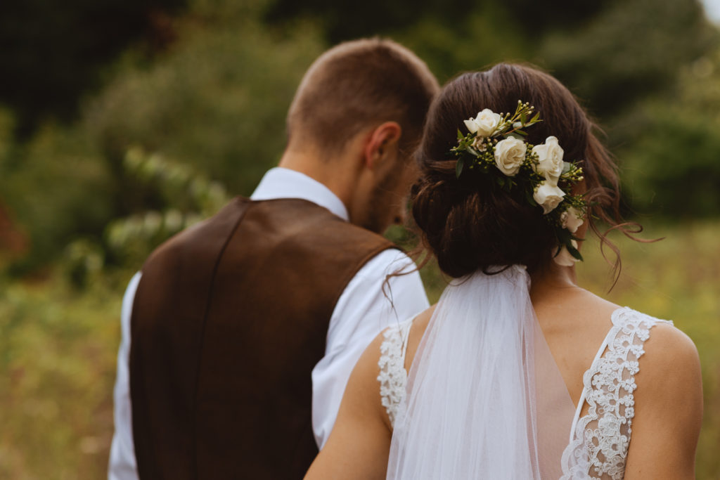 flowers in bride's hair with veil as she walks with her groom