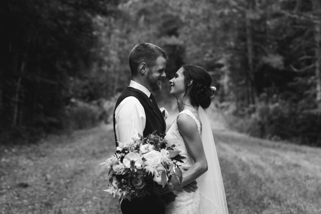 black and white photo of bride and groom standing on a path surrounded by trees