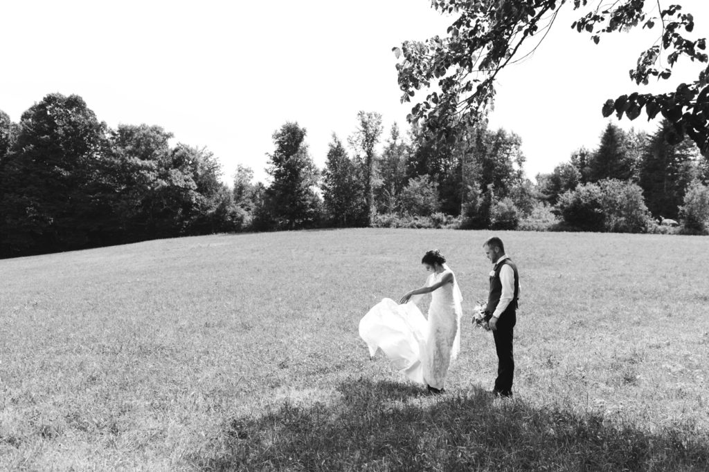 black and white photo of bride fixing her train in a hay field