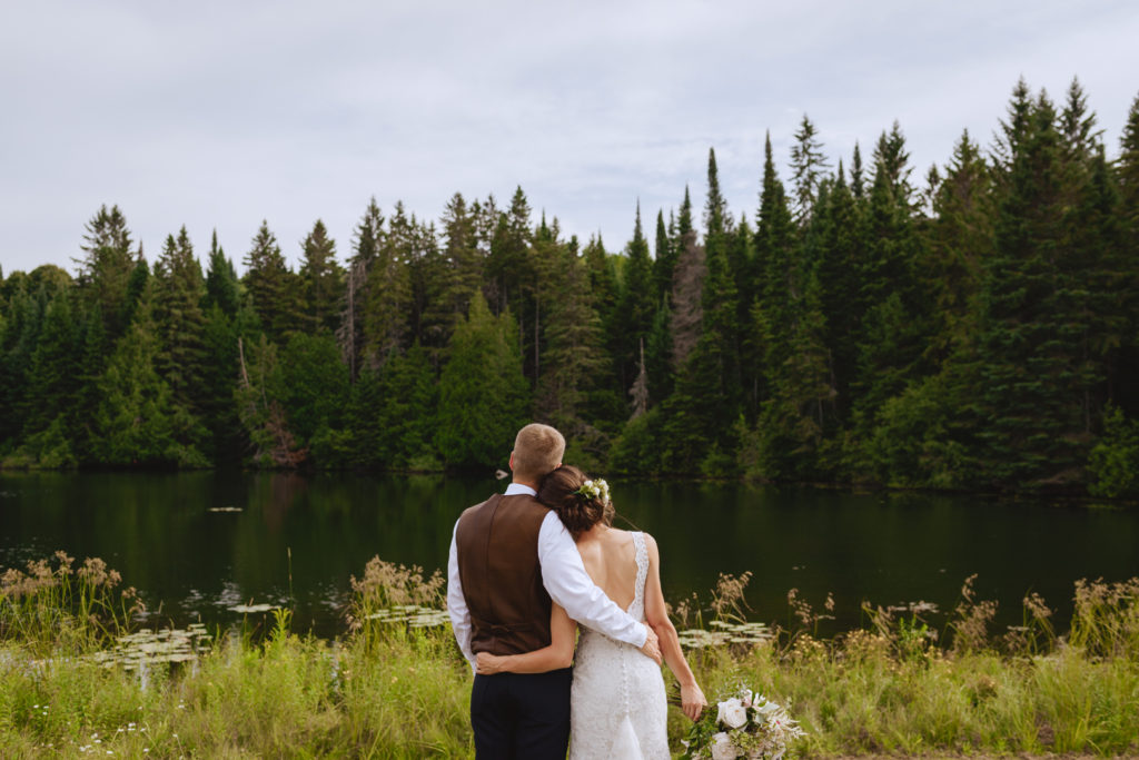 bride and groom looking out onto the water with evergreen trees
