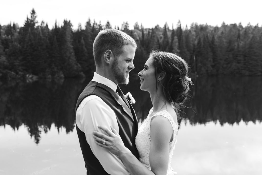 back and white photo of bride and groom with tree line reflected in the water